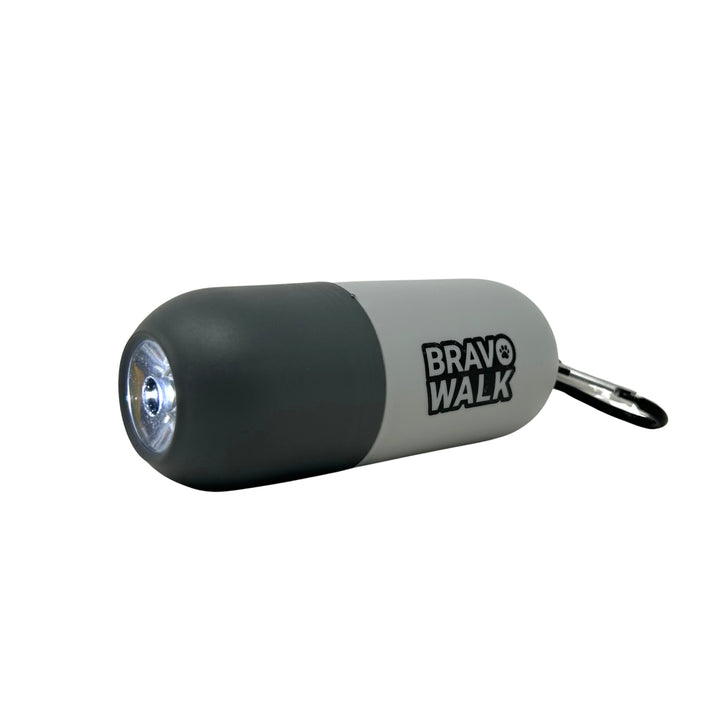 A cylindrical gray BravoWalk poop bag dispenser with a built-in flashlight at one end, and a carabiner clip on the other, against a white background.